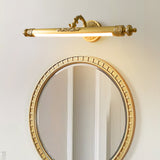Brass bar lit above an oval gold framed mirror on a pale bedroom wall