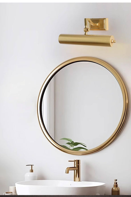 Brass tube above a round mirror over a white basin with a gold tap