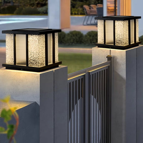 Lit cubes on pillars beside a pool with planting behind them at dusk