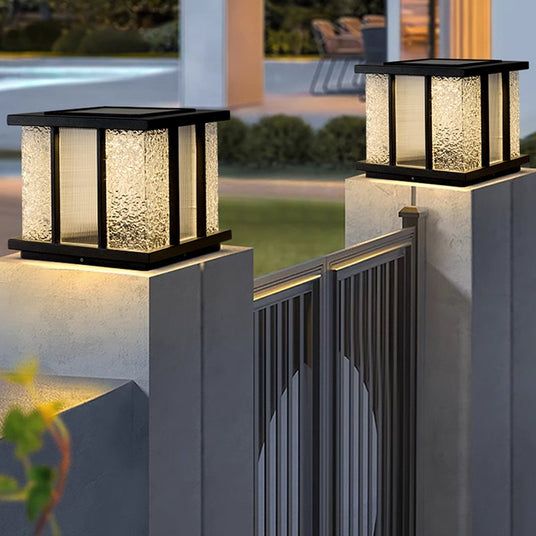 Lit cubes on pillars beside a pool with planting behind them at dusk