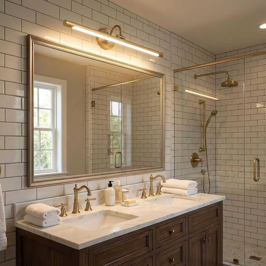 Brass bar lit above a wide mirror over a double basin vanity in a tiled bathroom