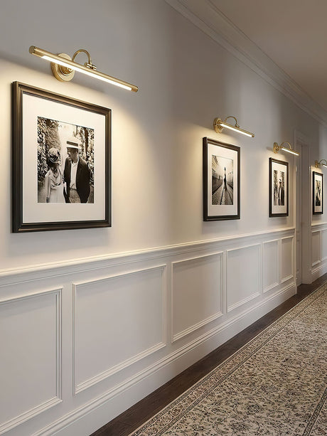 Brass bars lit along a hallway of framed photographs above wood wainscoting