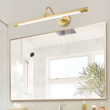 Brass bar lit above a wide framed mirror in a white bathroom beside a window