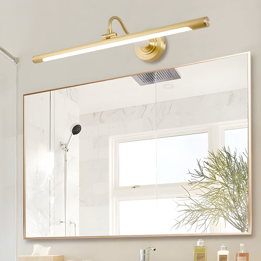Brass bar lit above a wide framed mirror in a white bathroom beside a window