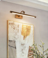 Bronze bar lit over a gilt framed canvas beside a branch of small leaves