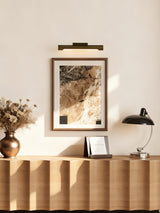 Bronze bar lit over a framed print above a fluted console with flowers