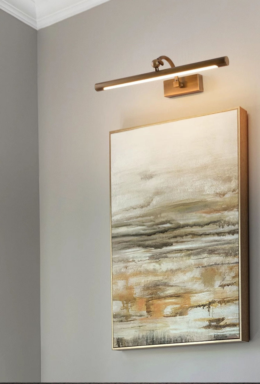 Bronze bar lit above a tall framed canvas on a pale wall seen from the side