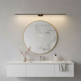 Slim rod lit above a round brass mirror over a white vanity unit with a towel