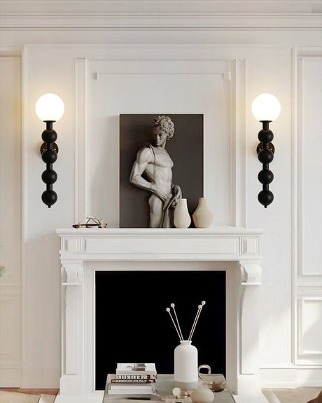 Two sconces lit either side of a mantel holding a small stone sculpture
