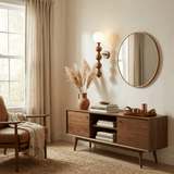 Two sconces lit above a long wood sideboard between two bright windows