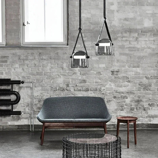 Two bucket shades on straps above a gray sofa against a brick wall