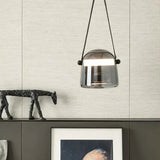 A hand holding the smoke shade by its leather strap beside an artwork