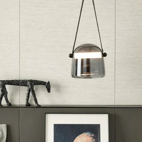 A hand holding the smoke shade by its leather strap beside an artwork