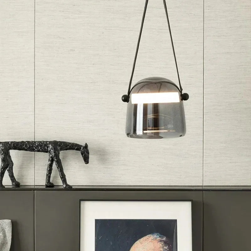 A hand holding the smoke shade by its leather strap beside an artwork