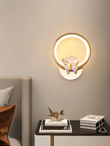 The butterfly ring lit above a nightstand with a bird figurine beside a gray headboard