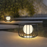 The cage lantern lit on wide concrete steps with planting beside them