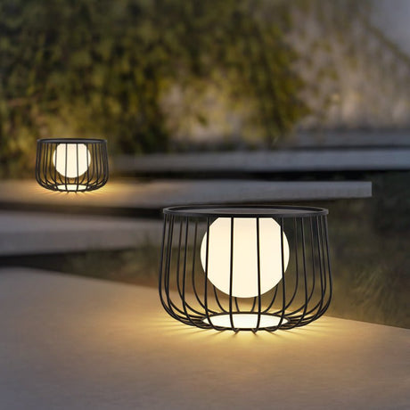 The cage lantern lit on wide concrete steps with planting beside them