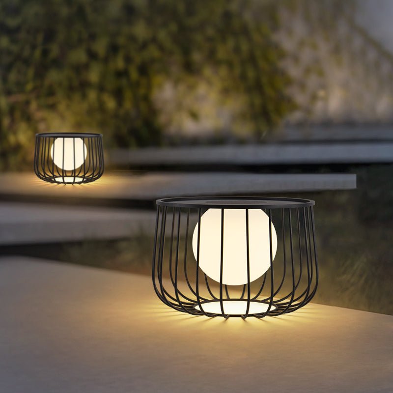 The cage lantern lit on wide concrete steps with planting beside them