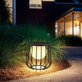 The cage lantern lit among ornamental grasses at the edge of a path