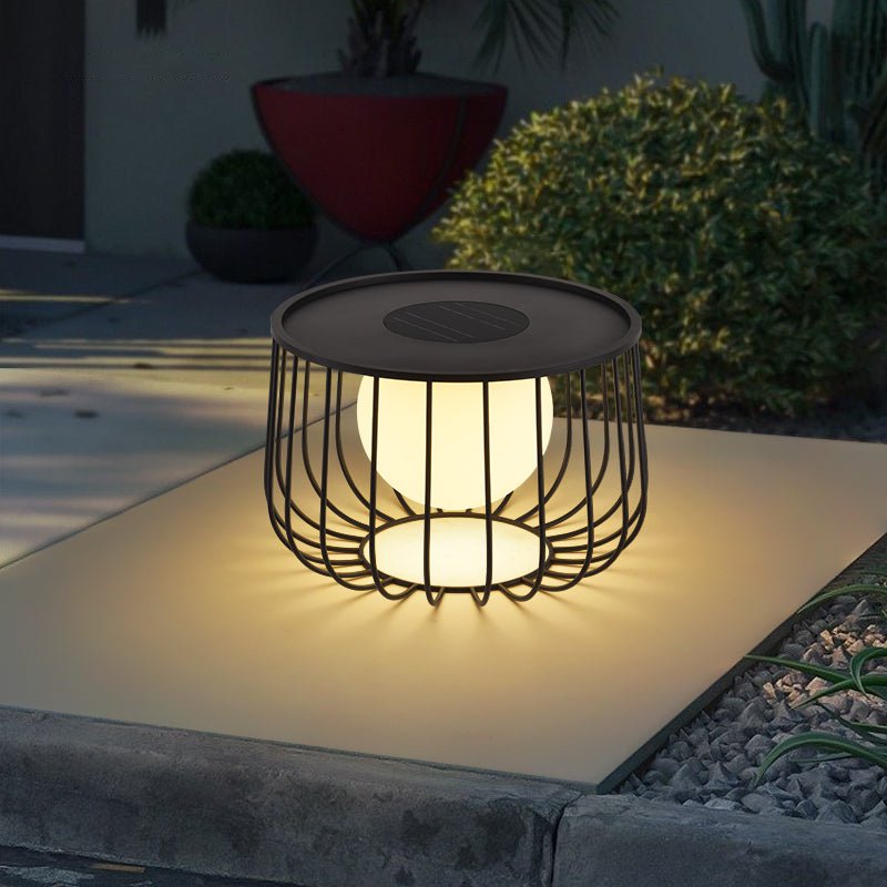 The lantern lit on paving beside clipped shrubs and a planted border