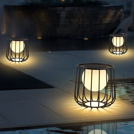 A run of cage lanterns lit on paving along the edge of a dark pool