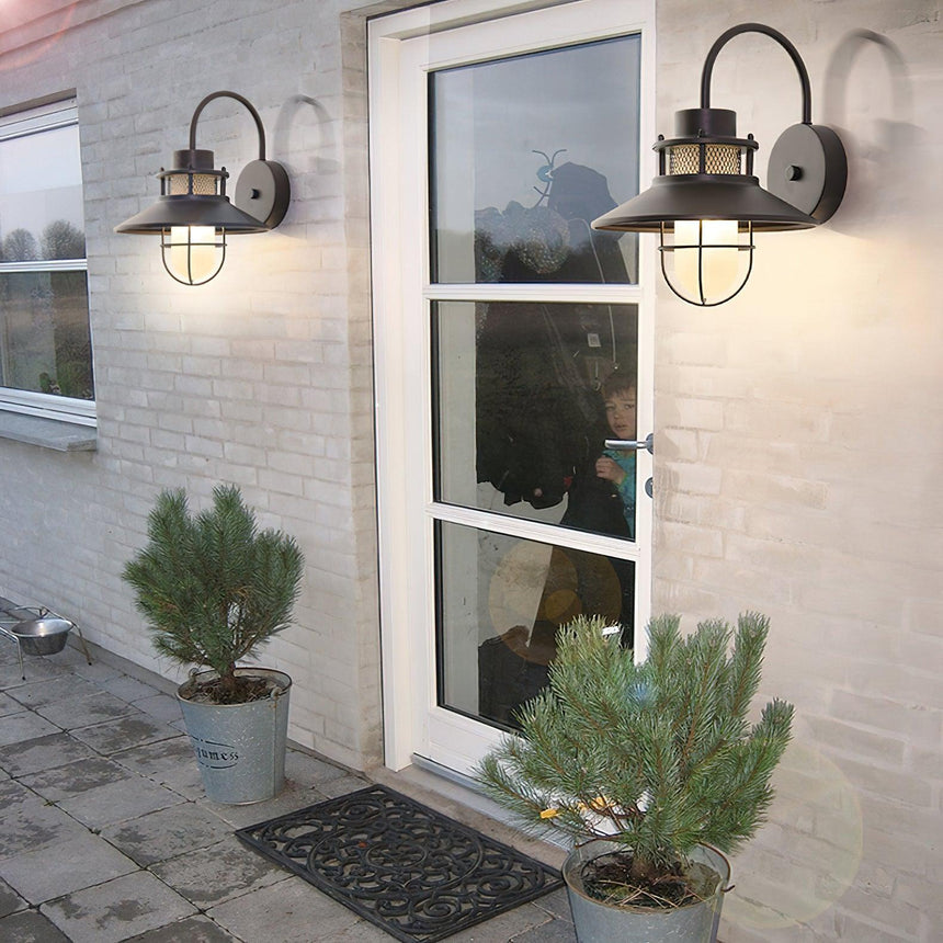Two sconces on a white brick wall on either side of a glass door with potted pines