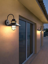 Sconces lit on a stucco wall beside sliding patio doors under a deep eave