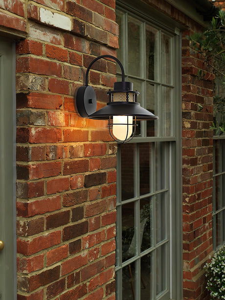 The sconce lit on red brick beside a green framed window