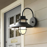 The sconce lit beside a pale gray front door with a brass mail slot
