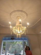 Seen from below against a plaster ceiling rose with a window beyond