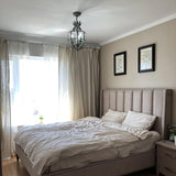 Hung in a bedroom above a made bed with long curtains and framed prints