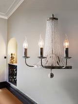 The three arm sconce lit on a white wall beside an arched niche and a paneled doorway