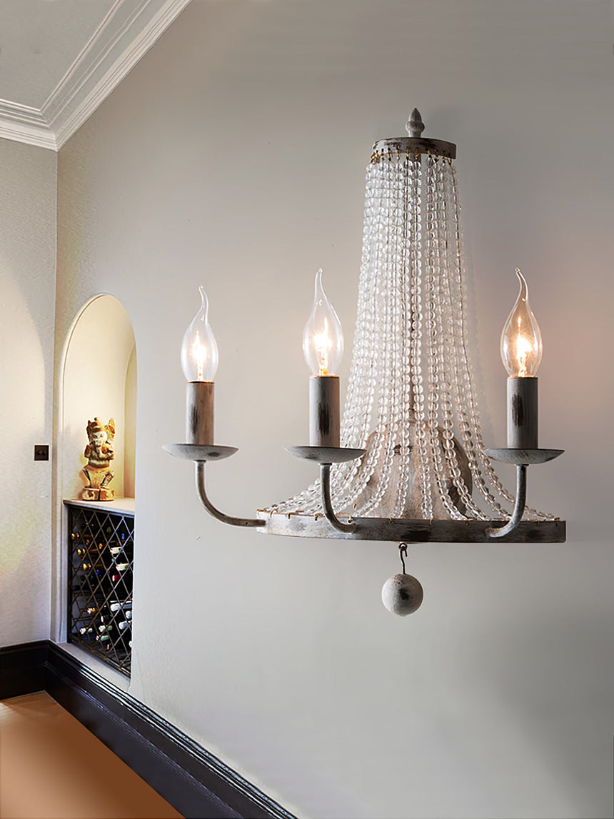 The three arm sconce lit on a white wall beside an arched niche and a paneled doorway