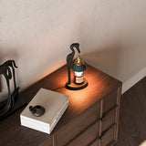 Heron lamp lit on a dark chest beside a book and a small speaker