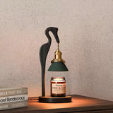 Heron lamp lit on a console beside a book and a paint color box