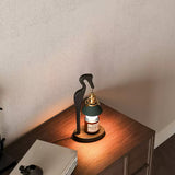 Heron lamp lit on a desk beside a laptop and a pale wall