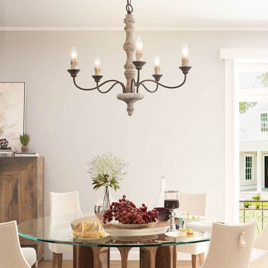 The chandelier lit over a round glass dining table with a bowl of fruit and pale chairs