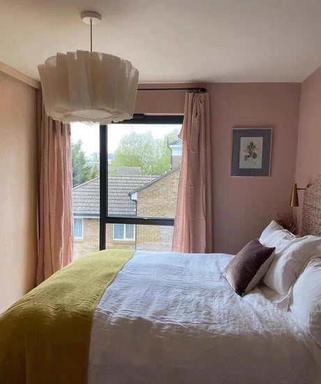 Pleated fabric shade lit in a bedroom beside long curtains
