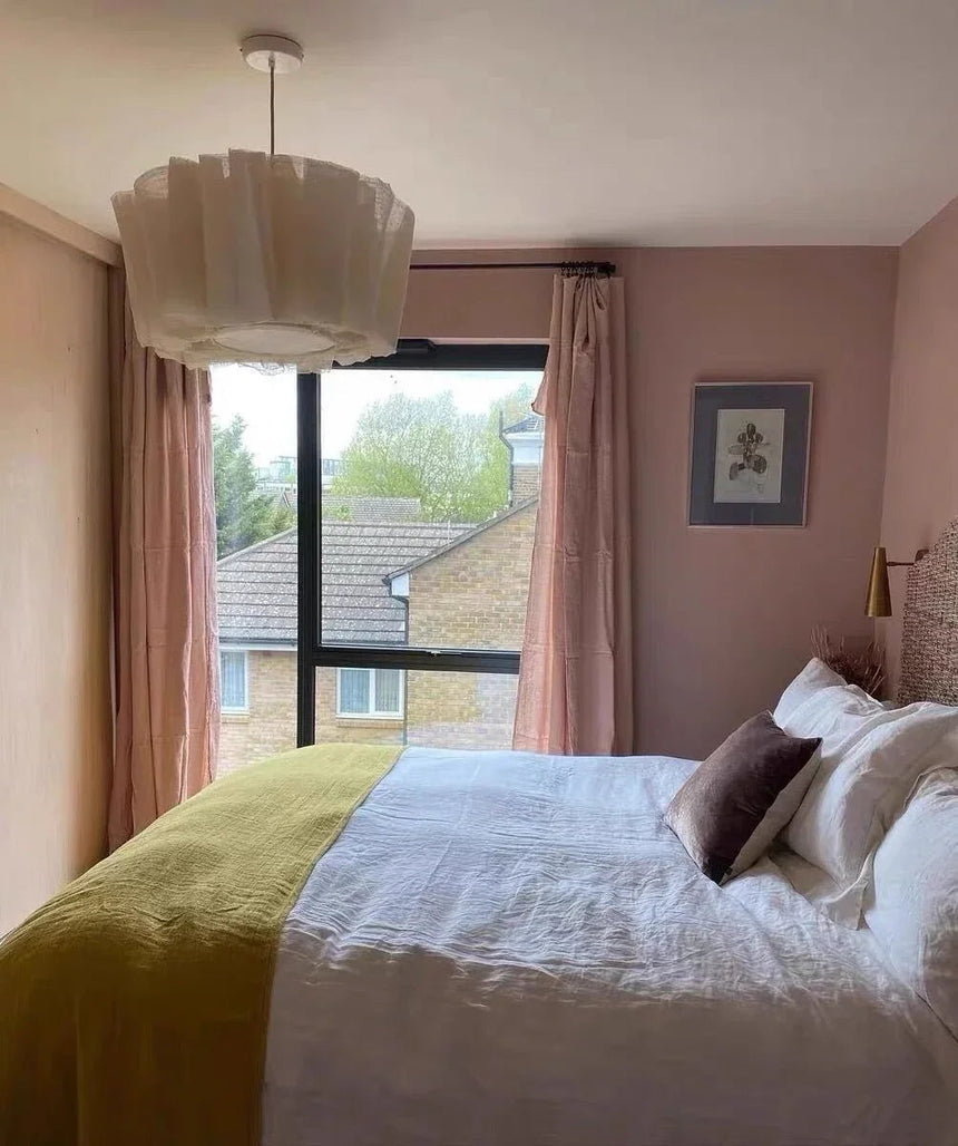 Pleated fabric shade lit in a bedroom beside long curtains