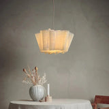 Pleated fabric shade lit against a gray wall with dried stems below