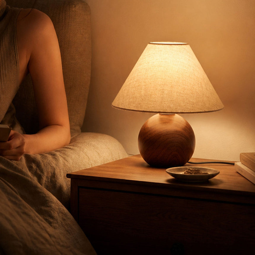 Ceramic bedside lamp lit on a nightstand beside a linen headboard