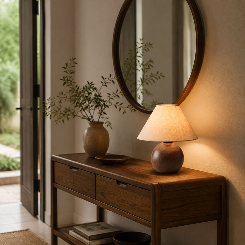 Ceramic bedside lamp lit on a console beside a round mirror and greenery