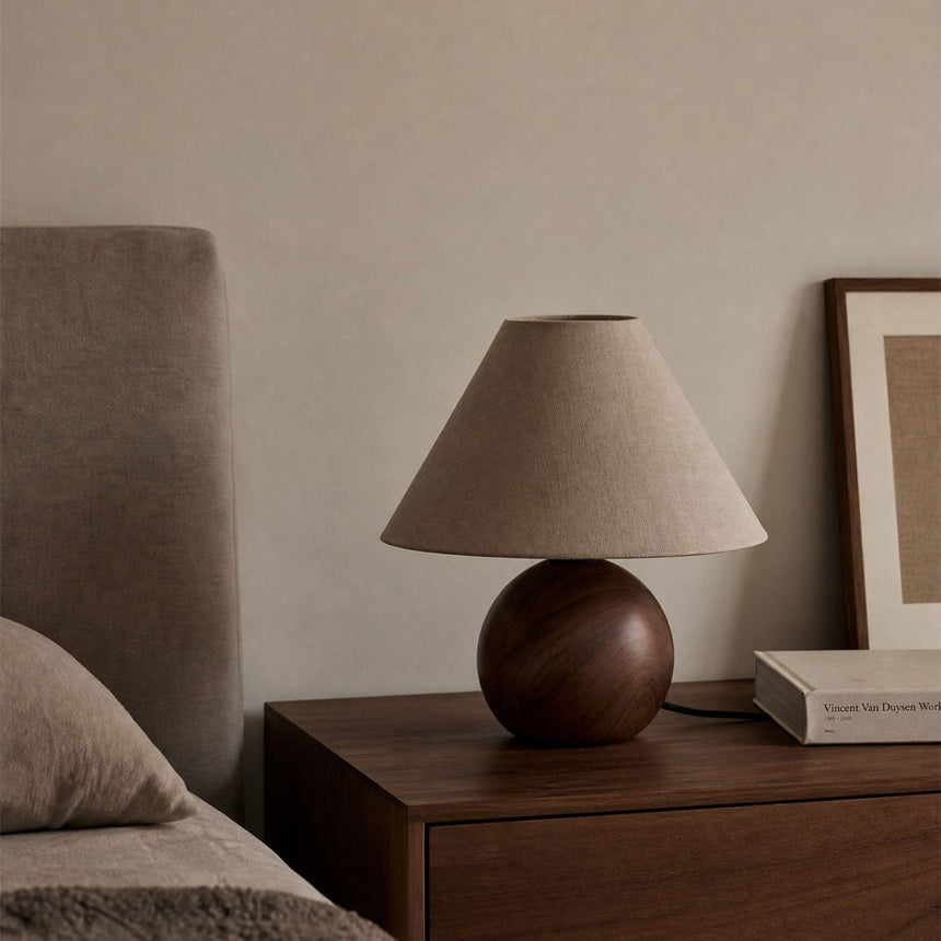 Ceramic bedside lamp unlit on a nightstand beside a framed print