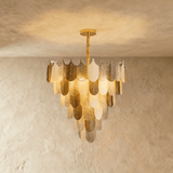 A round chandelier of tiered gold and white feather shaped glass shades, lit