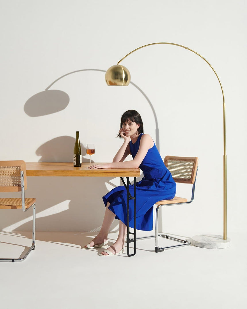 Brass arc lamp over a wood table and chairs, someone seated at the desk