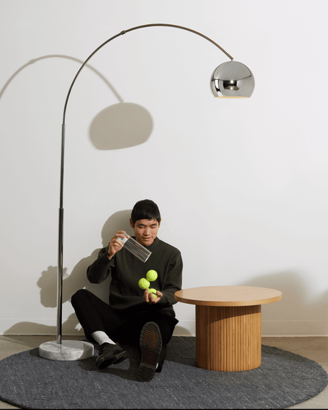 Chrome arc lamp over a round wood table on a gray rug in a bare room