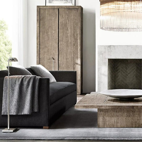 The lit lamp beside a dark sofa with a throw, a fireplace and a low table beyond
