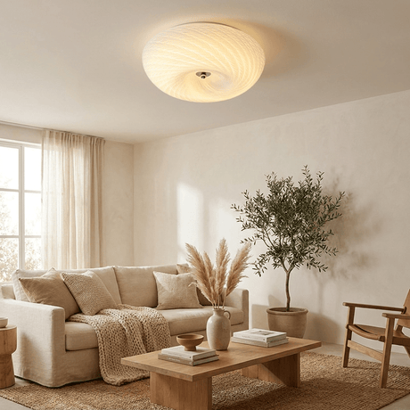 Swirled glass ceiling light lit in a living room with a pale sofa and an olive tree