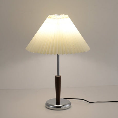 Chrome table lamp lit and seen from the side, pleats catching the light