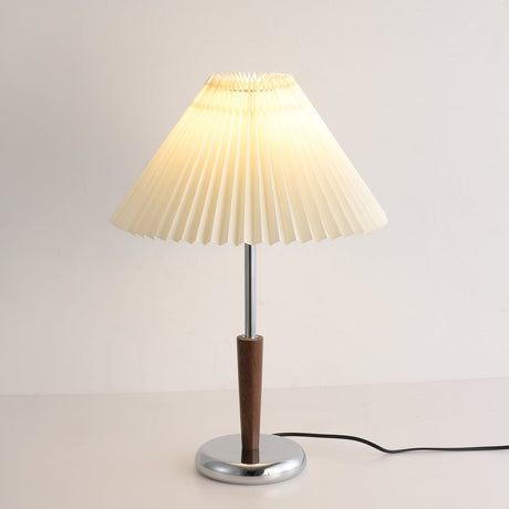 Chrome table lamp lit against a warm toned wall, shade glowing